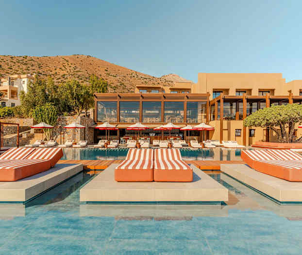 Et luksuriøst hotelkompleks med pool, liggestole og en bjergrig baggrund. (AI-genereret tekst)