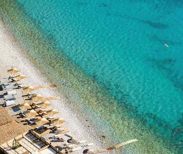 Udsigt over en strand med parasoller og liggestole ved klart blåt vand. (AI-genereret tekst)