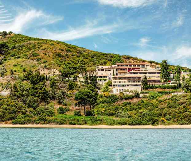 Hotelkompleks ved en grøn skråning nær vand. (AI-genereret tekst)