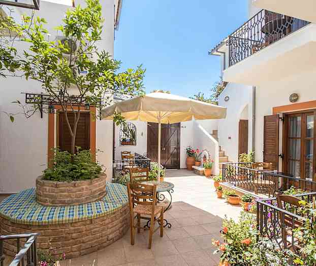 Inde gårdhave med blomsterkrukker, træer og havemøbler under en parasol. (AI-genereret tekst)