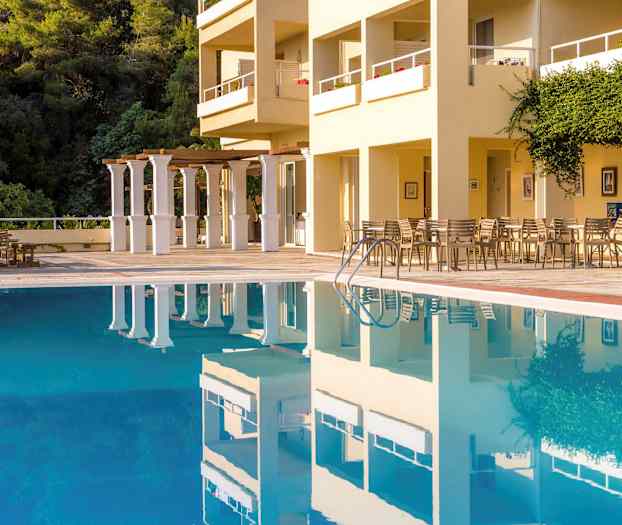 En udendørs pool foran en bygning med siddepladser og vegetation. (AI-genereret tekst)