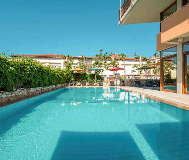 Udendørs swimmingpool omgivet af grønne områder og møblerede områder. (AI-genereret tekst)