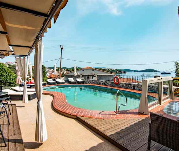 En pool med omkringliggende liggestole og udsigt over havet. (AI-genereret tekst)