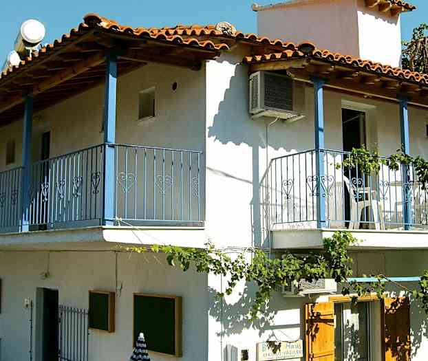 En toetagers bygning med hvid facade, blå altaner og røde tegltag. (AI-genereret tekst)