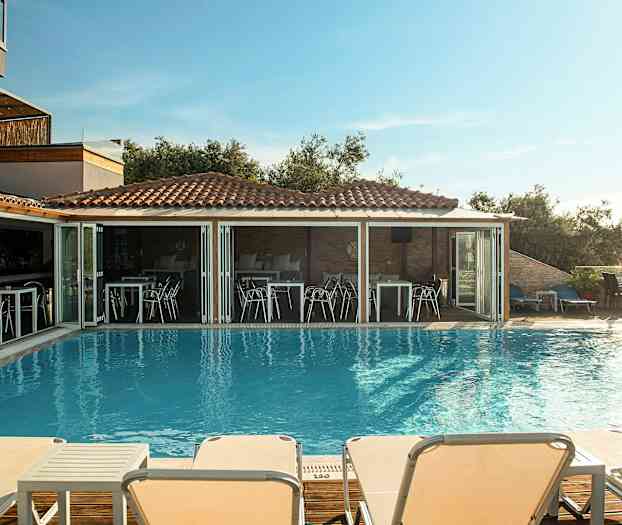 Udendørs swimmingpool med liggestole og en restaurant i baggrunden. (AI-genereret tekst)