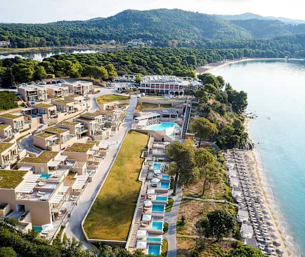 Luftfoto af et strandnært hotel med pools og liggestole. (AI-genereret tekst)