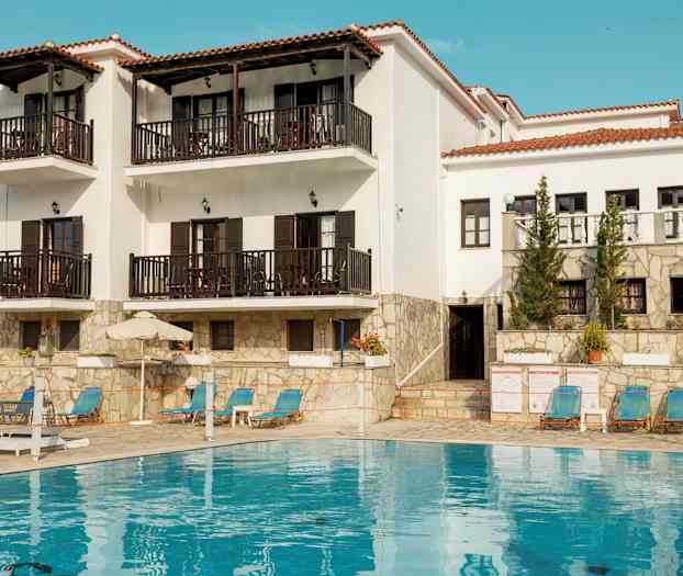 Hvid bygning med altaner og en pool foran. (AI-genereret tekst)