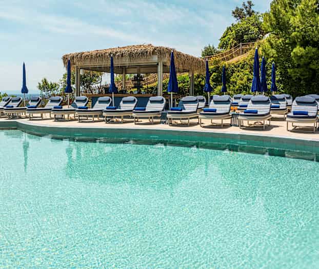 Pool med liggestole og parasoller. (AI-genereret tekst)