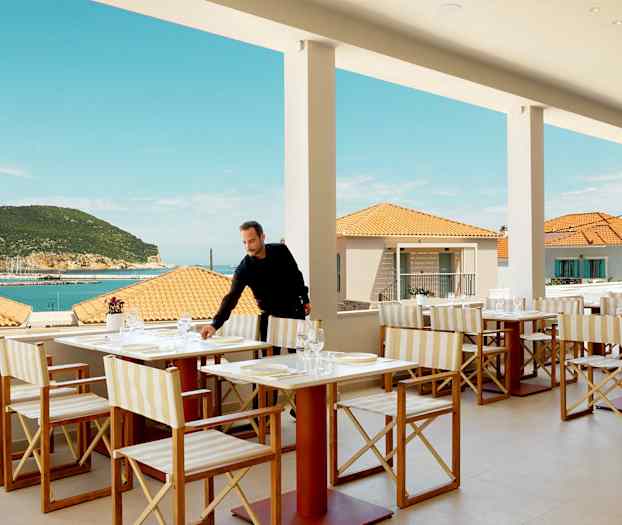 Restaurant med bordopstilling, udsigt over havet og terrasse, med baggrund af terrakottatag og en frodig bakke. (AI-genereret tekst)