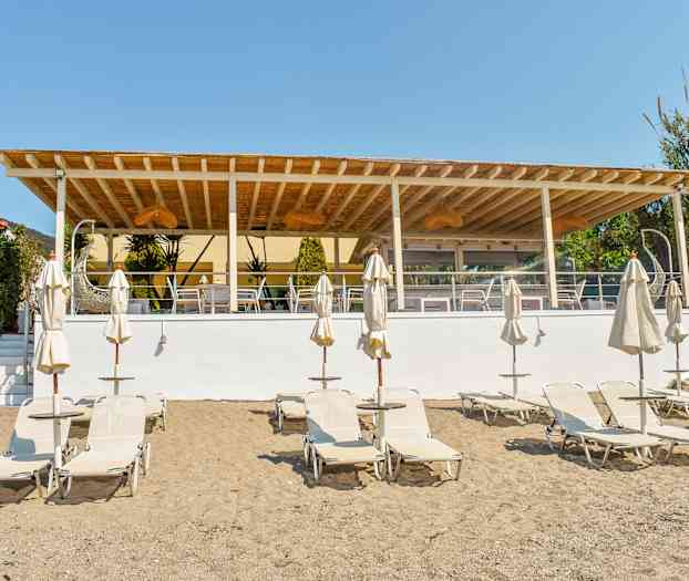 Strand med liggestole og parasoller foran en udendørsterrasse. (AI-genereret tekst)