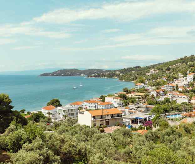 Udsigt over en kystby med huse, træer og hav. (AI-genereret tekst)