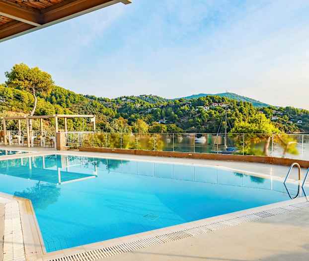 Et udendørs poolområde med udsigt over grønne bakker og en rolig sø. (AI-genereret tekst)