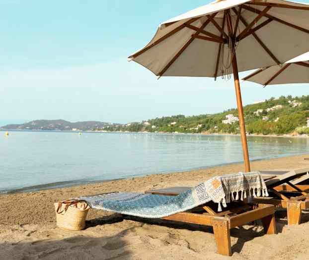 Strand med liggestole og store parasoller samt havudsigt. (AI-genereret tekst)