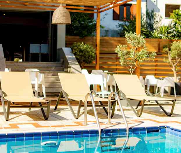 Tre liggestole ved en pool med borde og stole i baggrunden. (AI-genereret tekst)