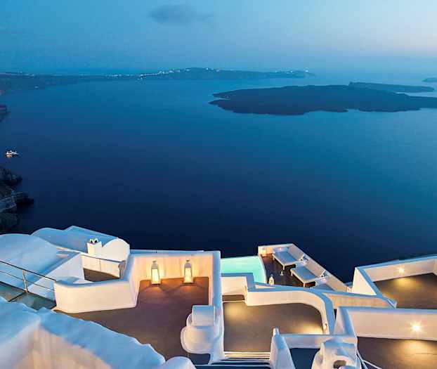 En udsigt ved skumring med hvide bygninger tæt på vand og bjerge. (AI-genereret tekst)