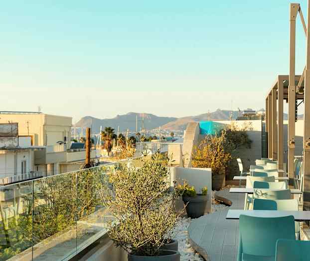 Billede af en tagterrasse med siddepladser og beplantning, med udsigt over byen og bjerge i baggrunden. (AI-genereret tekst)