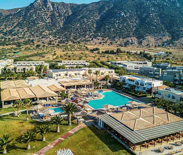 Billede af et feriested med swimmingpool og omkringliggende bygninger, beliggende nær et bjergrigt landskab. (AI-genereret tekst)