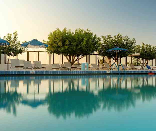 Udendørs pool omgivet af træer, parasoller og liggestole. (AI-genereret tekst)