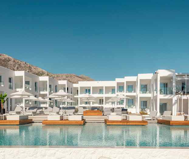 Hvid hotelbygning med udendørs pool og liggestole. (AI-genereret tekst)