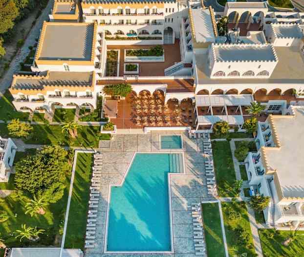 Luftfoto af et feriehotel med poolområde og omliggende bygninger. (AI-genereret tekst)