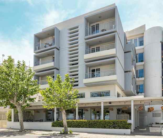 Moderne bygning med altaner og træer i forgrunden. (AI-genereret tekst)