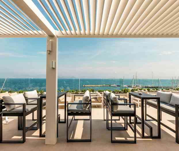 Udendørs servering med udsigt over havet, med sofaer og borde under en pergola. (AI-genereret tekst)