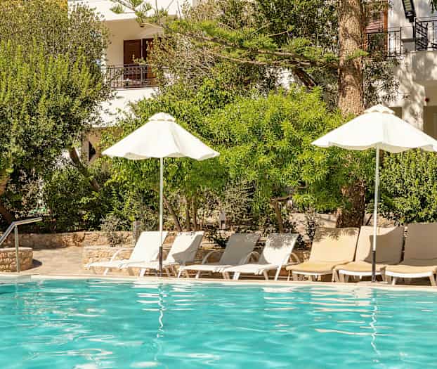 En udendørs pool med liggestole og parasoller omgivet af frodig beplantning. (AI-genereret tekst)