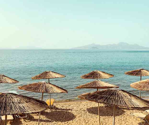 Strand med halmparasoller ved havet. (AI-genereret tekst)