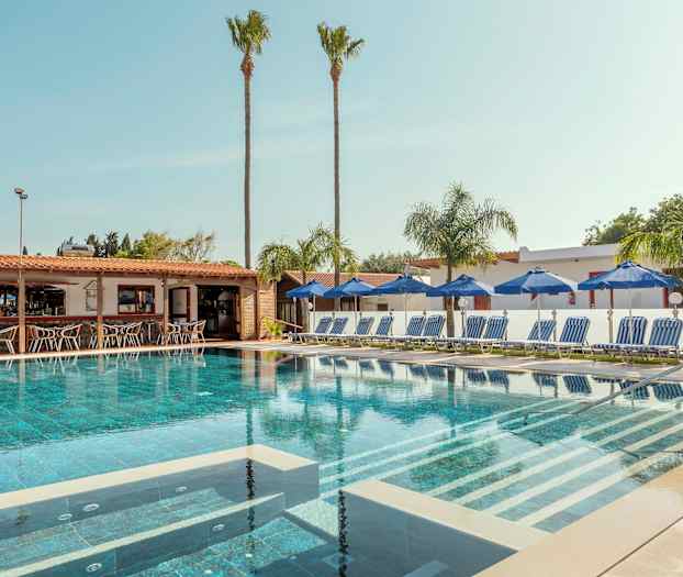 En pool omgivet af liggestole og parasoller med en bar i baggrunden. (AI-genereret tekst)