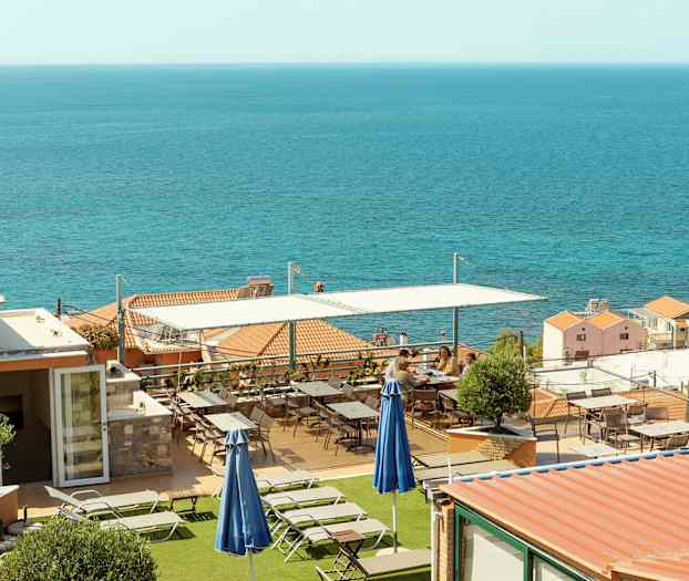 Terrasse med liggestole og borde, med havet i baggrunden. (AI-genereret tekst)