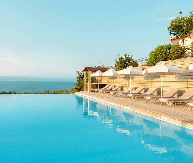 Udsigt over en infinitypool med liggestole og parasoller ved siden. (AI-genereret tekst)