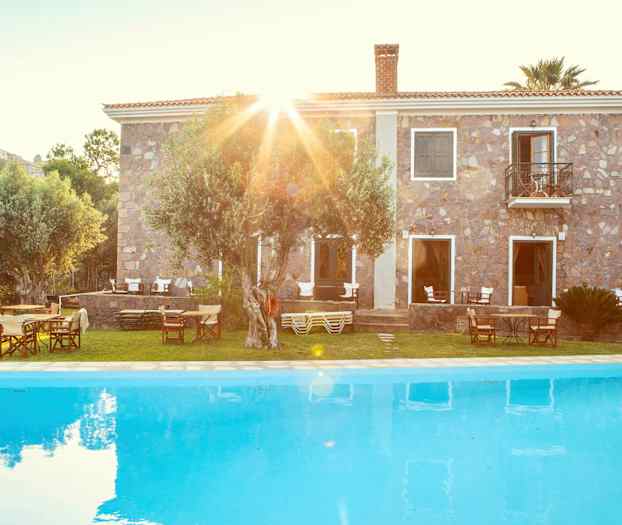 En stenbygning bag en pool med havemøbler og træer. (AI-genereret tekst)