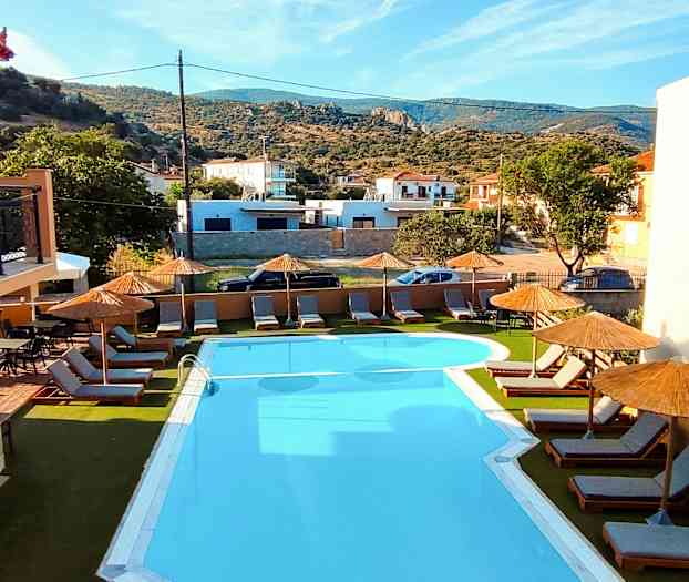 Udendørs swimmingpool med liggestole og parasoller, omgivet af vegetation og bygninger. (AI-genereret tekst)