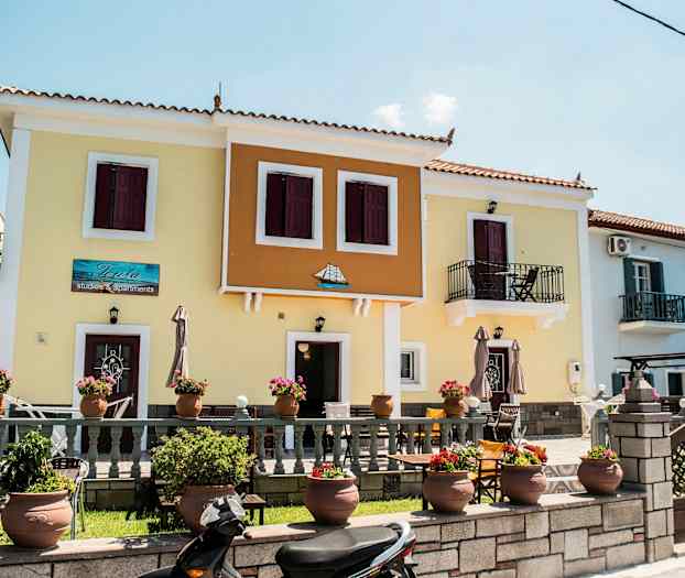 Farverigt hus med altaner og blomsterkrukker foran. (AI-genereret tekst)