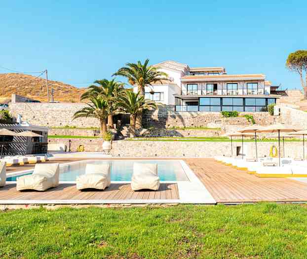 Et luksusresort med pool, liggestole og palmer foran en bygning. (AI-genereret tekst)