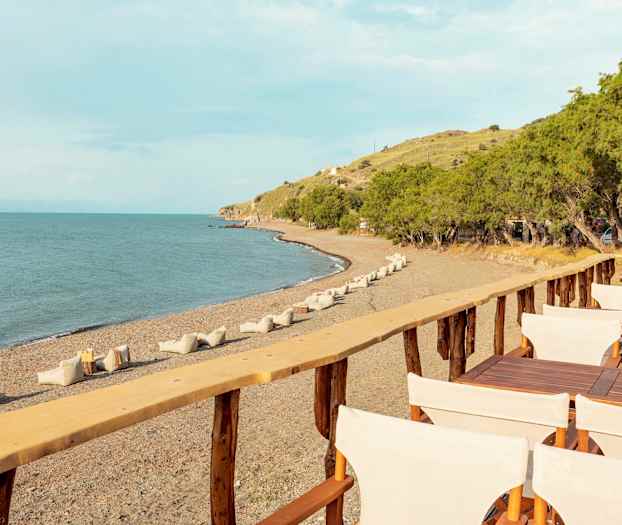 En strand med stole og borde på en træterrasse, træer i baggrunden. (AI-genereret tekst)