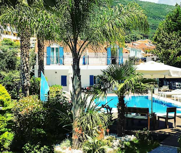 En have med palmer og planter omkring en pool foran en lys bygning. (AI-genereret tekst)