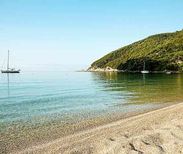 En stille strand med klart vand og sejlbåde i det fjerne. (AI-genereret tekst)