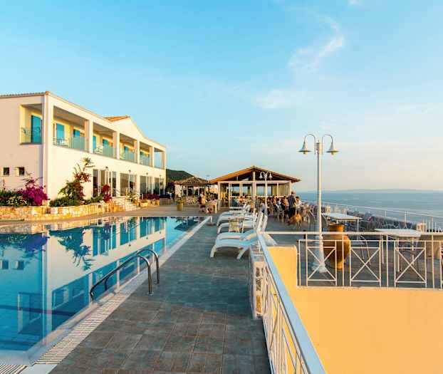 En hotelbygning ved en udendørs pool og en siddegruppe med udsigt over havet. (AI-genereret tekst)