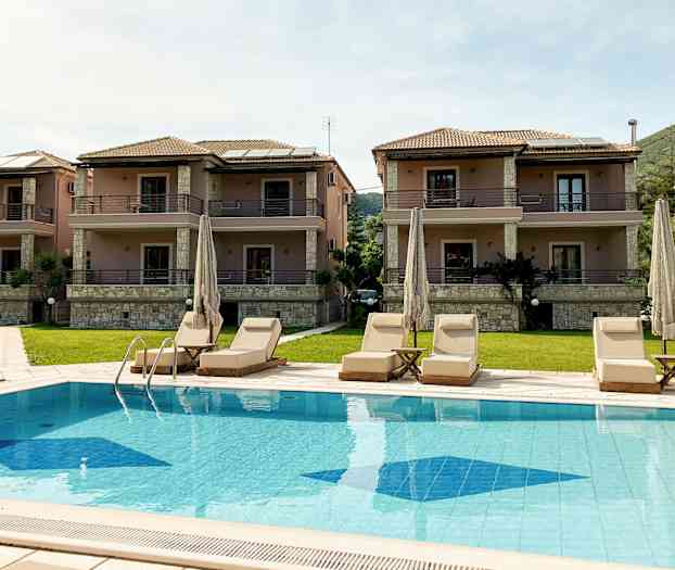 Tre bygninger med to etager og altaner samt en pool med liggestole foran. (AI-genereret tekst)