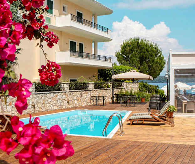 Billede af en bygning med altaner, en pool og møbler på en solterrasse med blomster i forgrunden. (AI-genereret tekst)