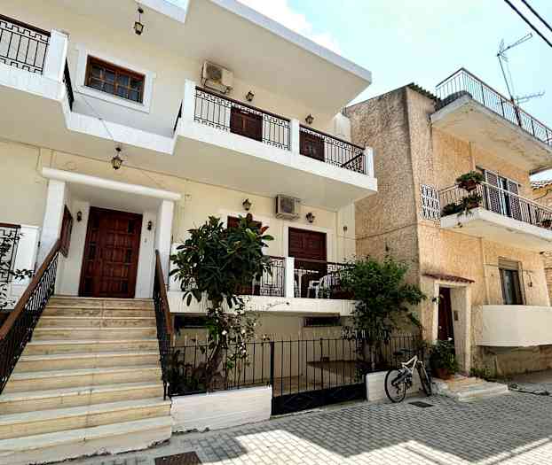 En bygning med flere etager, altaner og en have foran en brostensbelagt gade. (AI-genereret tekst)