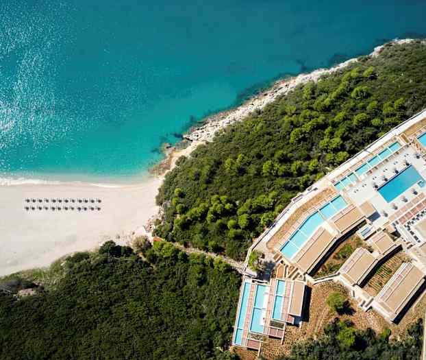 Luftfoto af en strand ved havet, omgivet af skov og et feriekompleks. (AI-genereret tekst)