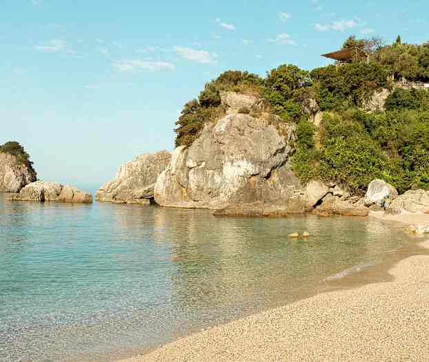 En strand med klart vand og klipper i baggrunden. (AI-genereret tekst)