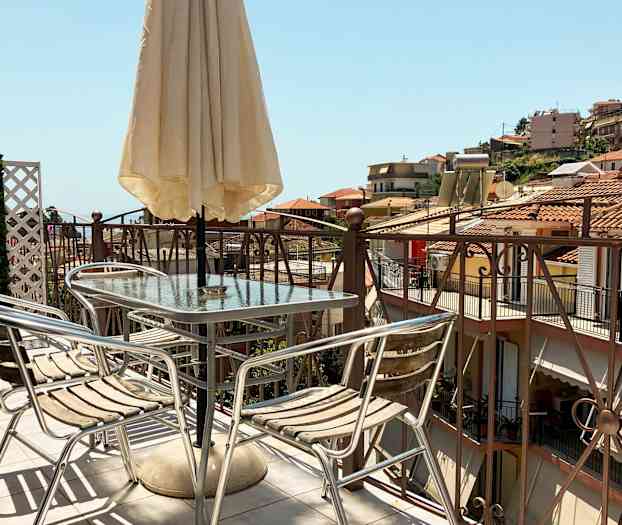 En terrasse med et bord, stole og parasol med udsigt over huse med tegltag. (AI-genereret tekst)