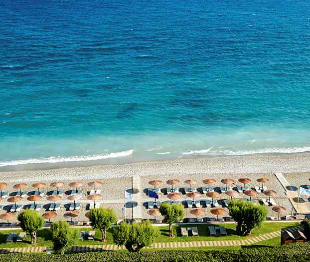 Udsigt over en strand med parasoller og liggestole mod et blåt hav. (AI-genereret tekst)