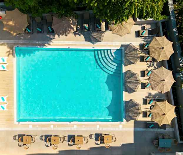 Billede af en udendørs swimmingpool omgivet af liggestole med parasoller og borde med stole. (AI-genereret tekst)