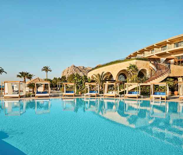 En udendørspool med liggestole og et hotel i baggrunden. (AI-genereret tekst)