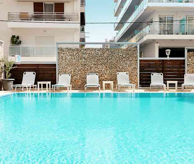 Swimmingpool med liggestole og borde foran bygninger. (AI-genereret tekst)