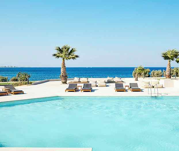 Poolområde ved havet med liggestole og palmer. (AI-genereret tekst)